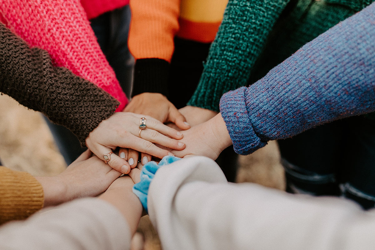 Eight Women in Sweaters Overlapping Their Hands in a Circle Finding Fellowship with Each Other
